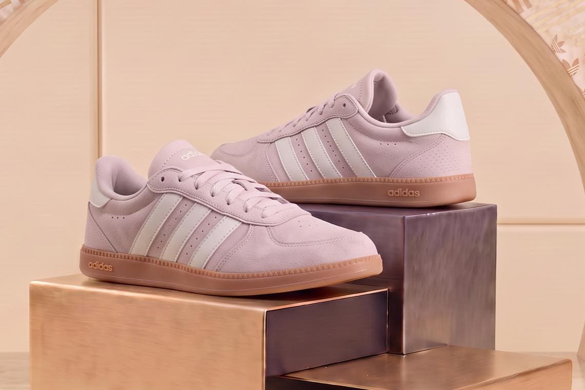 Adidas Sneaker in Beige mit weißen Streifen, seitlich auf glänzenden Podesten vor hellem Hintergrund präsentiert