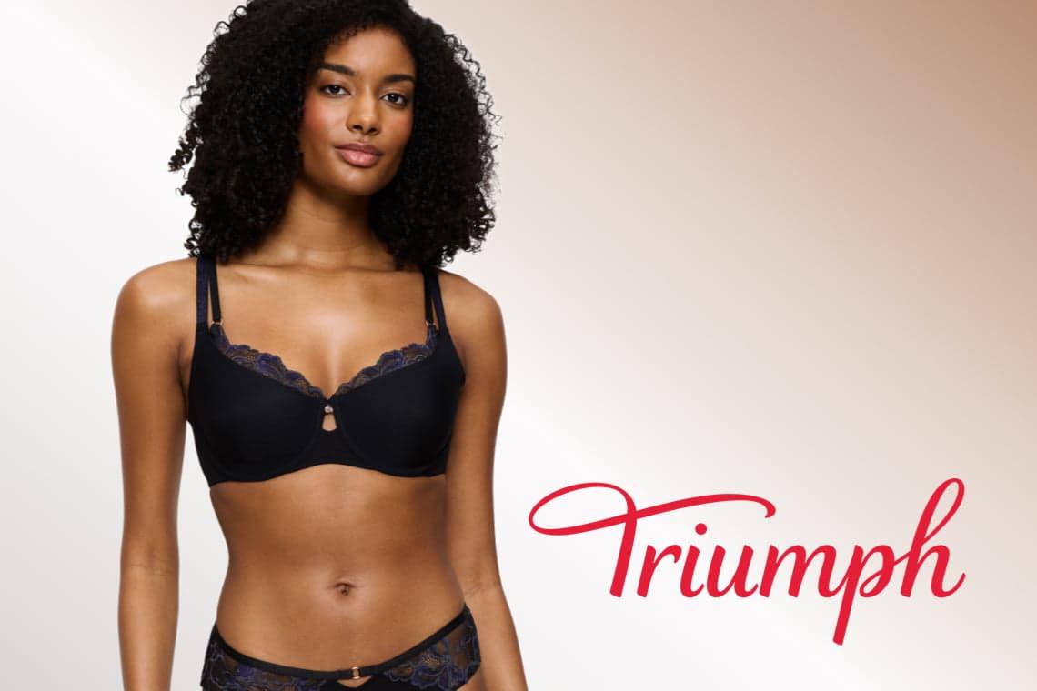 Triumph – Frau mit lockigem Haar trägt schwarzen BH und passende Slip im Halbporträt vor hellem Hintergrund