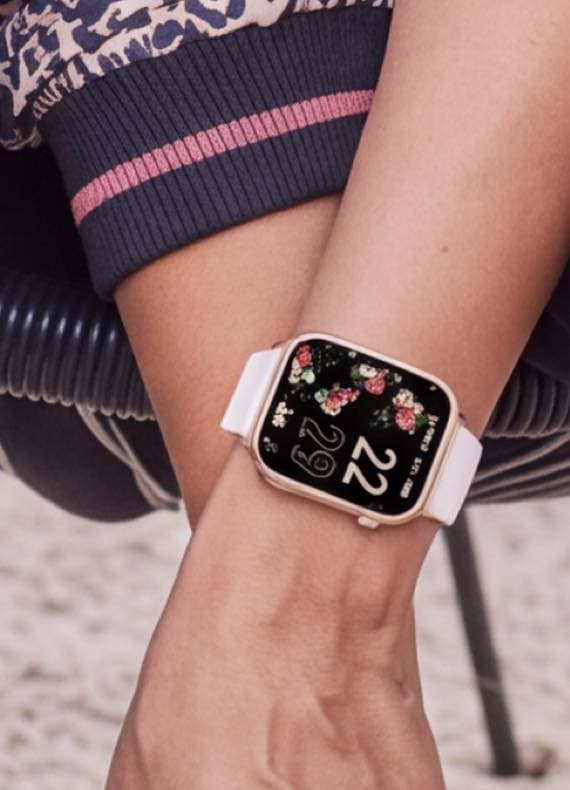 Smartwatch mit Blumen-Zifferblatt und weißem Armband am Handgelenk einer sitzenden Person