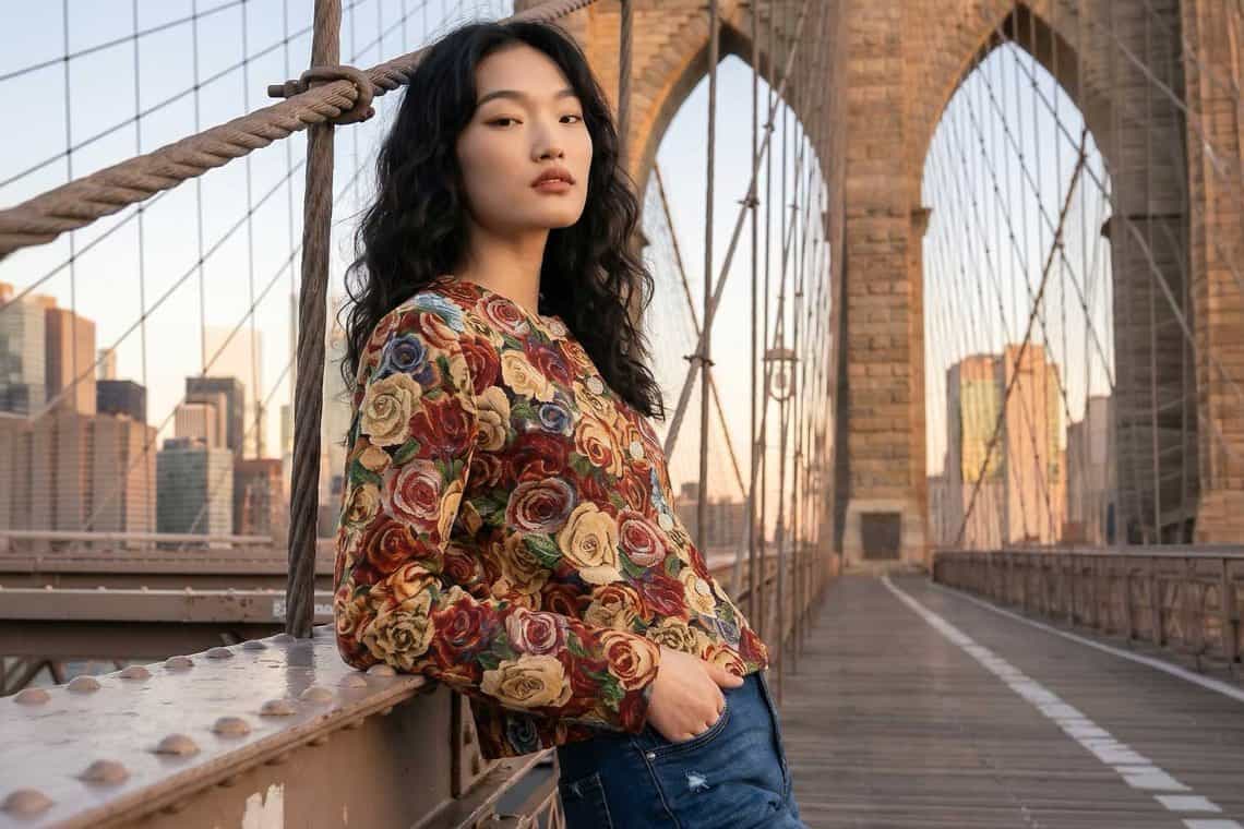 Frau in geblümtem Pullover steht auf einer Brücke und blickt zur Seite, Stadt mit Hochhäusern im Hintergrund
