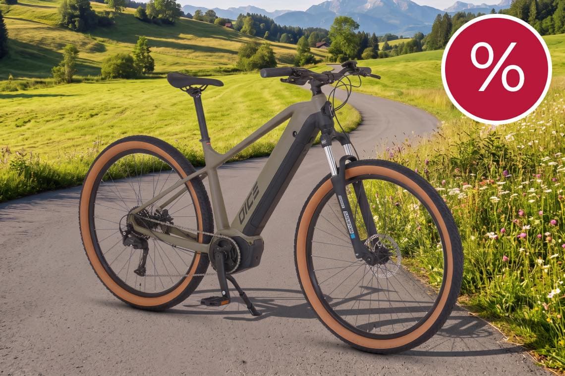 Prozentzeichen für Rabatt – E-Bike auf Landstraße vor grünen Hügeln und Bergen im Hintergrund
