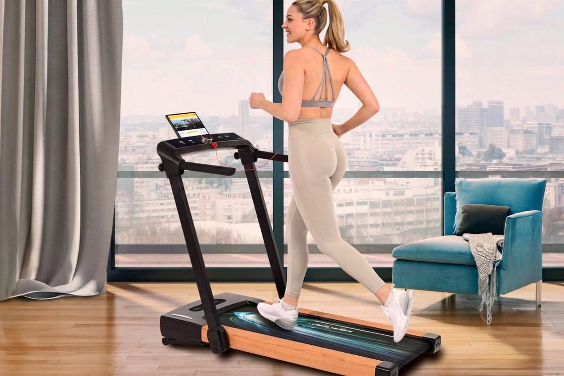 Frau in Sportkleidung joggt auf einem Laufband im Wohnzimmer vor großer Fensterfront mit Stadtblick