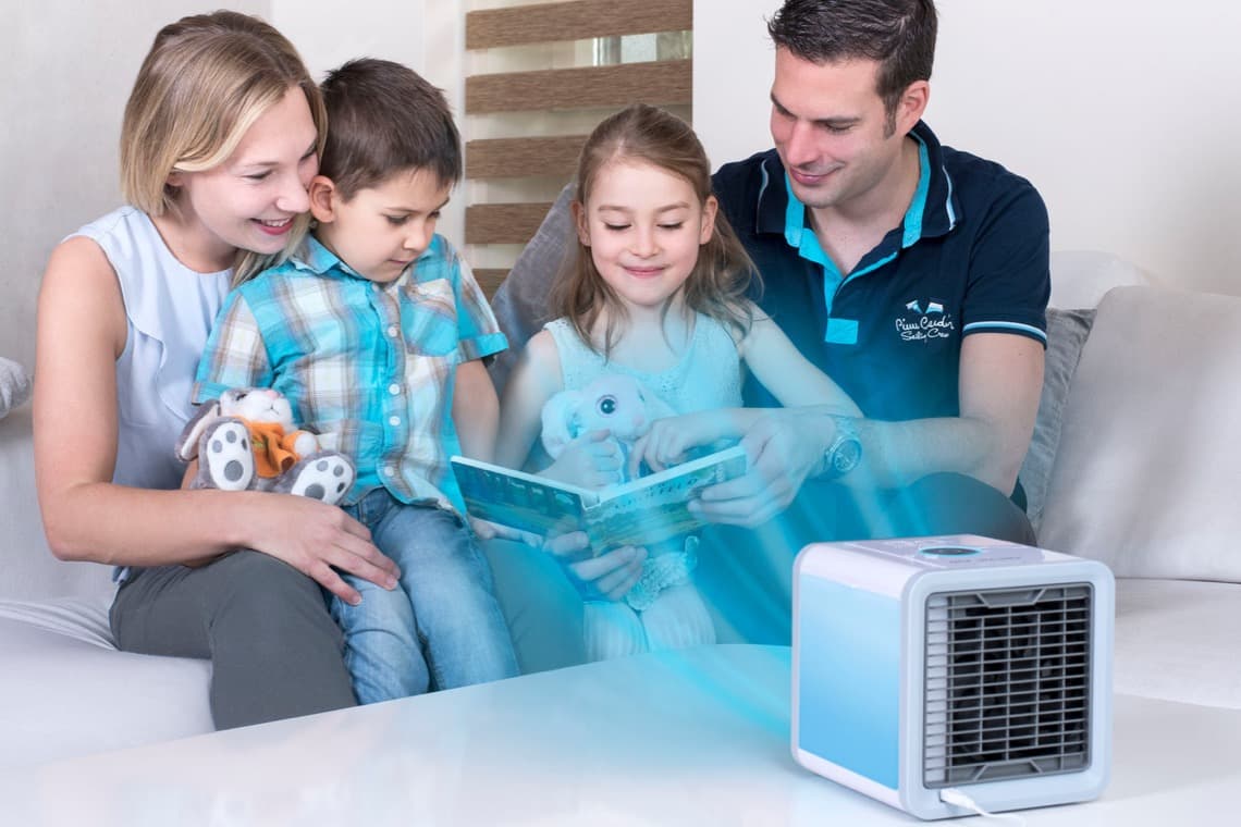 Eine Familie sitzt auf einem hellen Sofa und liest ein Buch. Neben ihnen steht ein kleiner, blauer Klimaanlagenapparat, aus dem Luft strömt.