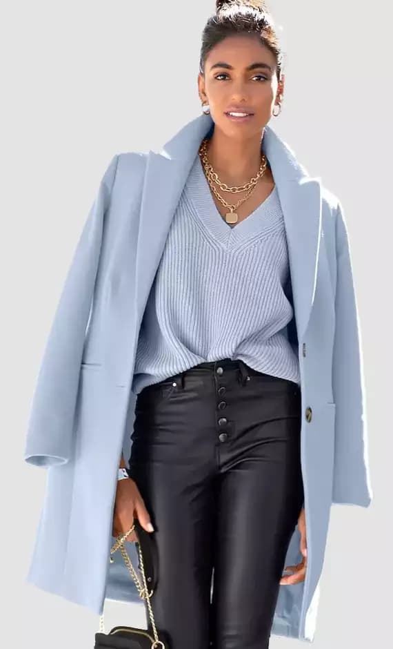 Frau trägt einen hellblauen, eleganten Mantel über blauem Pulli und Lederimitat-Jeans.