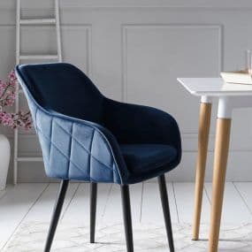 Blauer Polsterstuhl mit schwarzen Beinen neben einem weißen Tisch auf weißem Teppich.