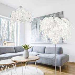 Modernes Wohnzimmer mit grauem Sofa, runden Holztischen und weißen Blütenlampen.