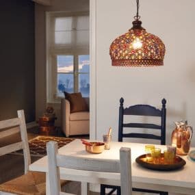 Esszimmer mit Mosaiklampe über Tisch, Tischgedeck und Stühle, im Hintergrund gemütlicher Wohnbereich mit Sessel