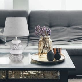 Tischlampe, Vasen und Dekoration auf einem Kaffeetisch vor grauem Sofa in modernem Wohnzimmer