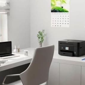 Modern Büroeinrichtung mit Laptop, Drucker, Kalender und Pflanze auf dem Schreibtisch.