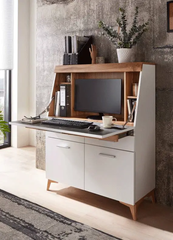 Kompakter Sekretär mit aufgeklappter Arbeitsfläche, Monitor, Tastatur, Ordnern und Pflanze vor Betonwand