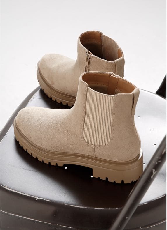Beige Chelsea-Boots mit Profilsohle stehen leicht versetzt auf einem dunklen Metallstuhl