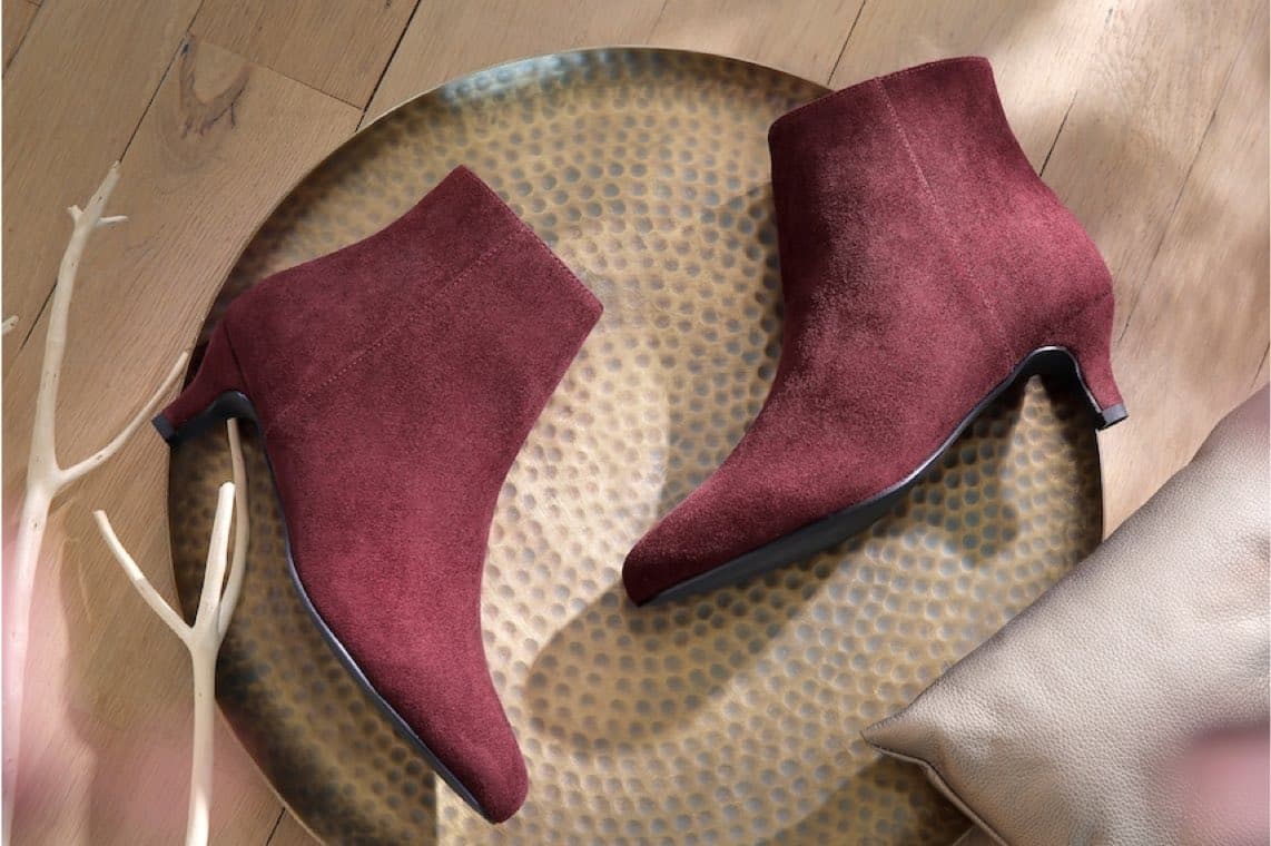 Bordeauxrote Stiefeletten mit kleinem Absatz liegen dekorativ auf rundem Metalltablett auf Holzboden