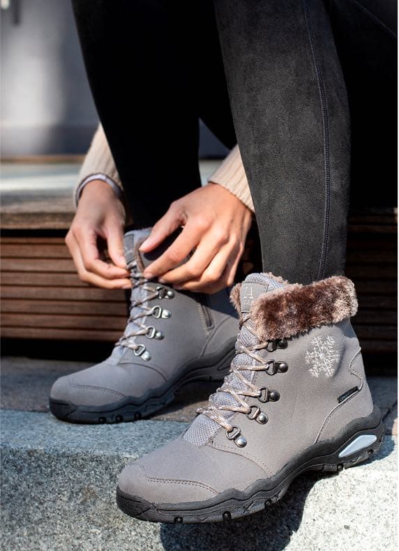 Person sitzt auf Stufe und schnürt graue Winterstiefel mit Fellrand und Schneeflockenmotiv an den Seiten