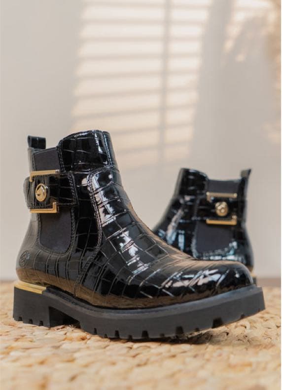 Schwarze knöchelhohe Stiefeletten mit Kroko-Struktur und goldener Schnalle, ein Schuh vorne, der andere im Hintergrund