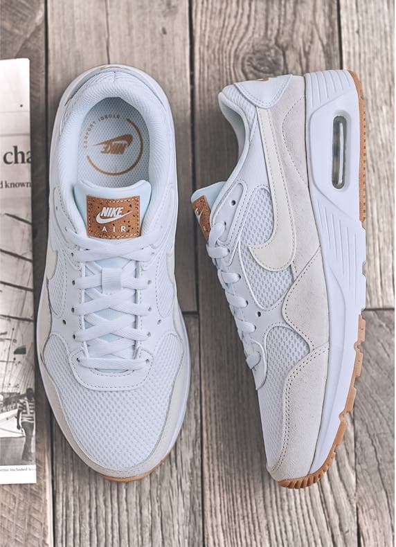 Weiße Nike Air Sneaker von oben, ein Schuh frontal, der andere seitlich auf Holzbohlen platziert