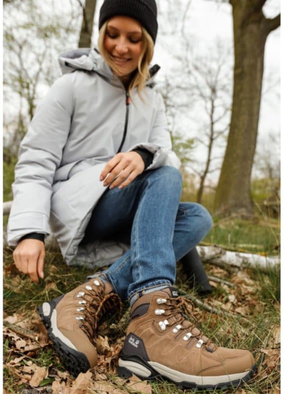 Frau im Park mit Mütze und Winterjacke sitzt im Laub und zeigt ihre braunen Wanderschuhe im Nahbereich