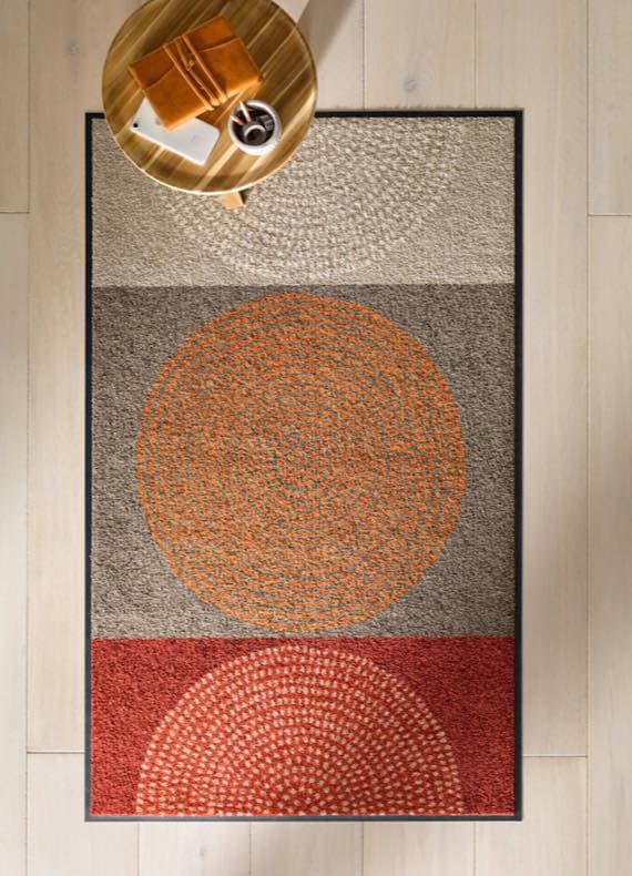 Rechteckiger Teppich mit drei großen Kreismustern in Beige, Orange und Rot, daneben runder Beistelltisch mit Tasse und Notizbuch