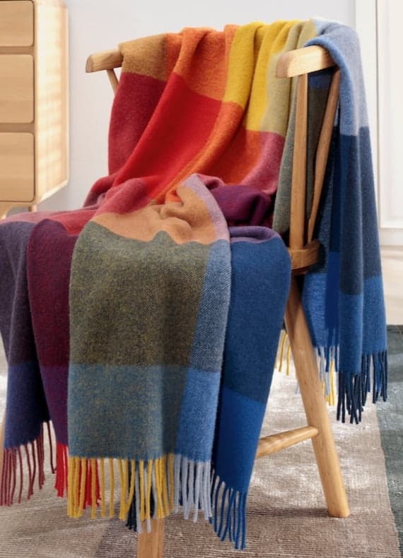 Bunte karierte Decke mit Fransen in Rot, Gelb, Blau und Lila locker über einen Holzstuhl gelegt