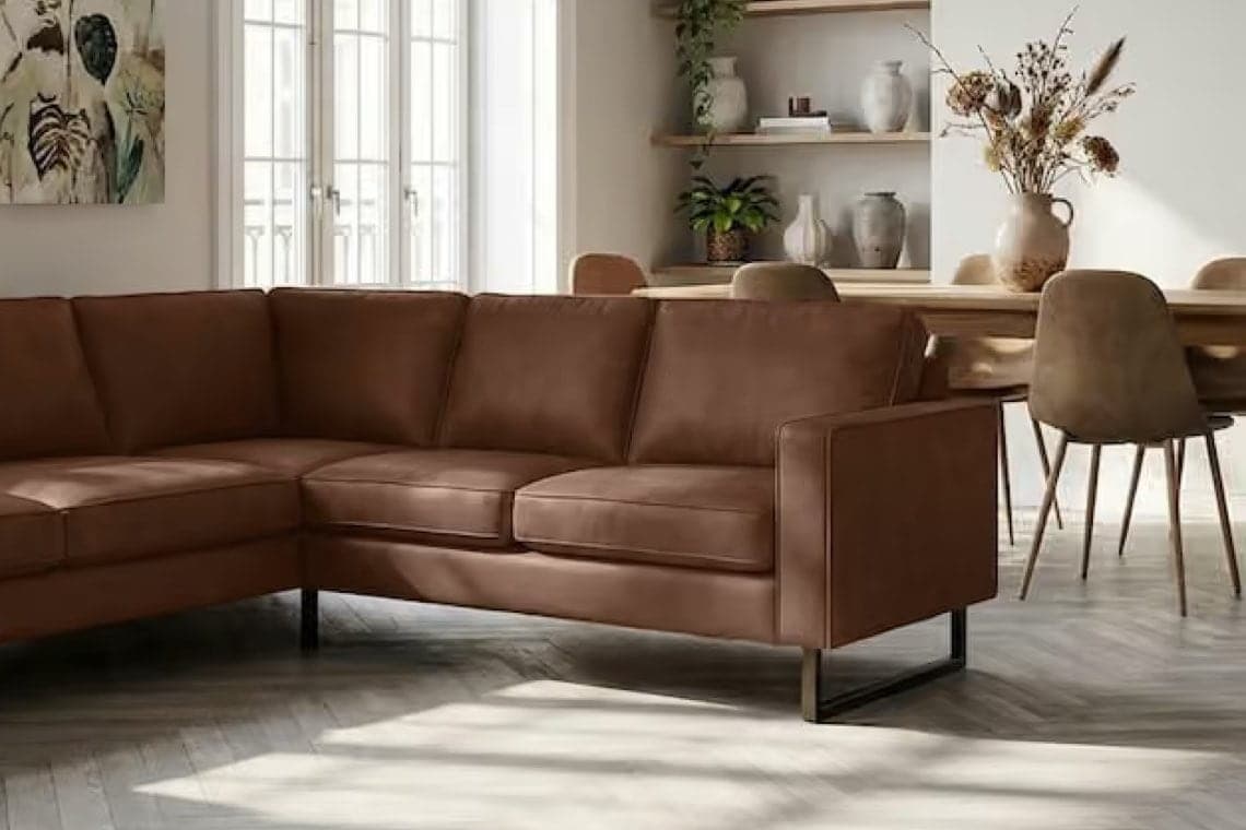 Ecksofa in Braun in hellem Wohnzimmer, dahinter Esstisch mit Stühlen, Regale mit Vasen und Pflanzen