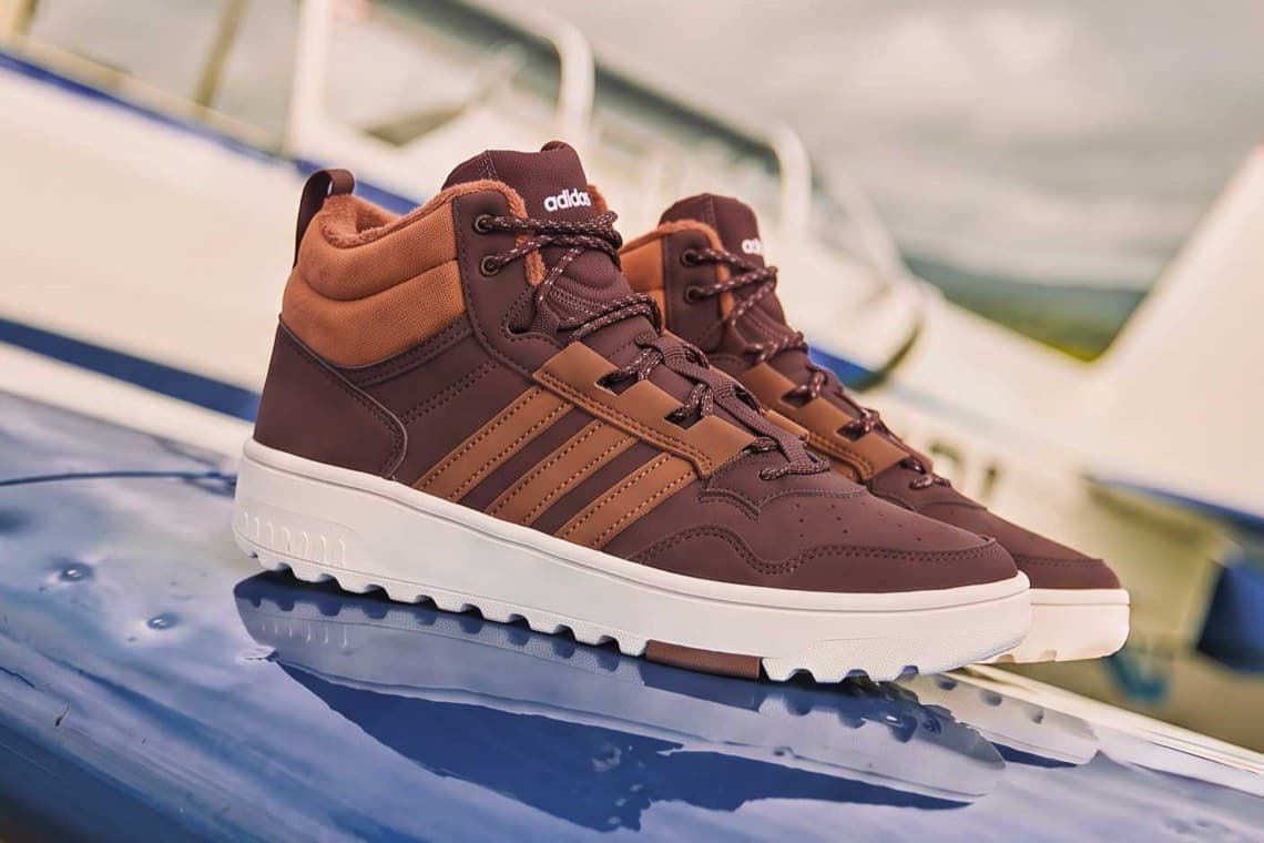 Braune adidas-Sneaker mit hohem Schaft und weißer Sohle stehen nebeneinander auf einer glänzenden Oberfläche draußen