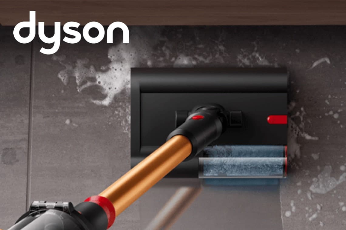 dyson – Akku-Staubsauger wischt nassen Schmutz von grauen Fliesen unter einem niedrigen Möbelstück