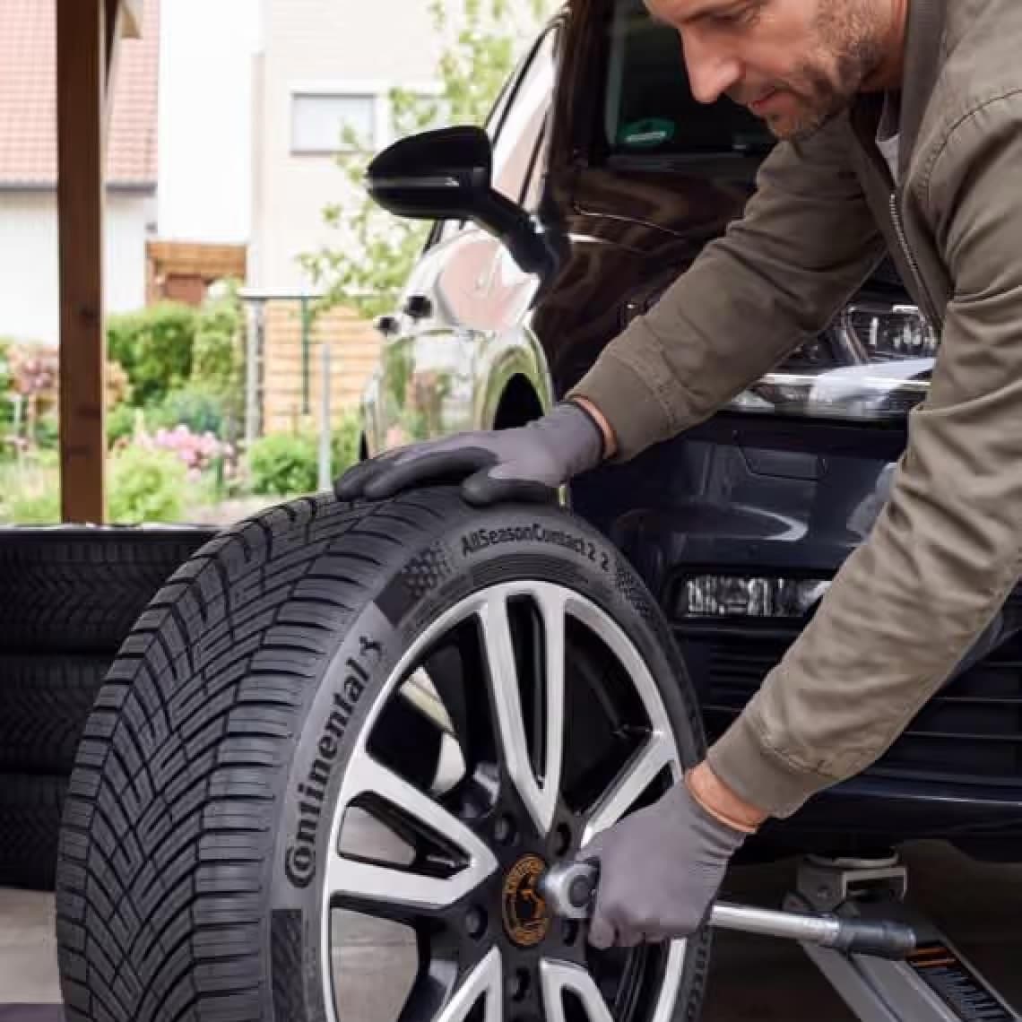 Mann montiert Continental-Autoreifen an einem angehobenen Auto und zieht die Radschrauben mit einem Werkzeug fest
