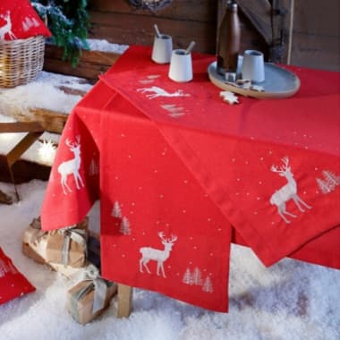 Rote Tischdecke mit weißen Rentier- und Tannenmotiven, aufgedeckter Wintertisch mit Geschenken im Kunstschnee