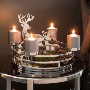 Runder Adventskranz mit vier brennenden Kerzen und silbernen Hirschfiguren auf einem Tisch