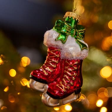 Weihnachtsbaumanhänger mit roten Schlittschuhen und grünem Schleifenband vor golden leuchtenden Lichtern
