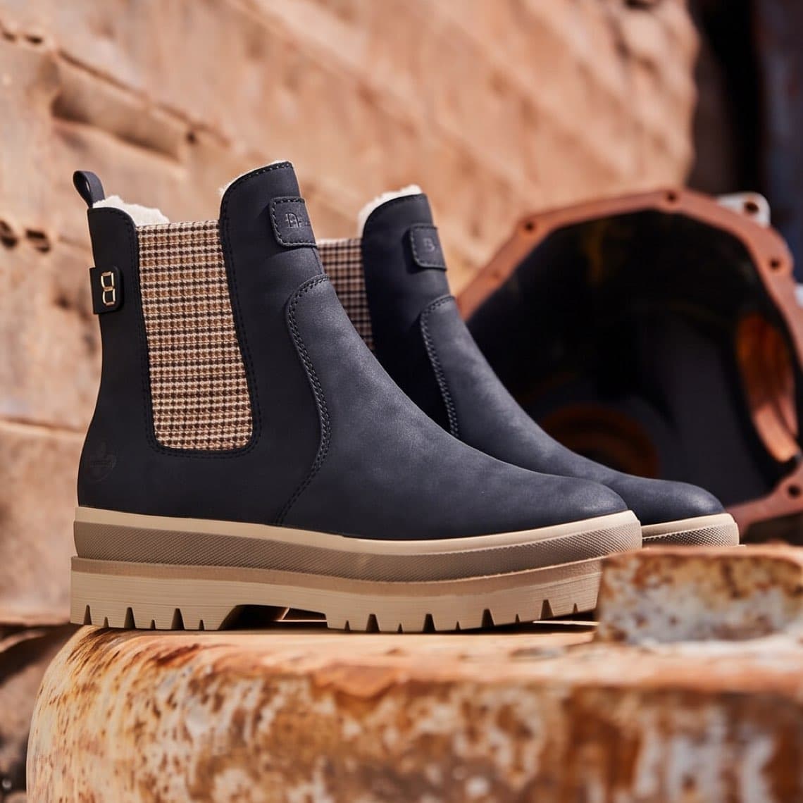 Dunkelblaue Chelsea-Boots mit hellen Blocksohlen und karierten Seiteneinsätzen auf rostigem Metallhintergrund