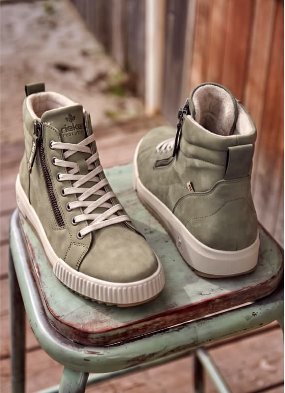 Hellgrüne knöchelhohe Sneaker mit Schnürung und seitlichem Reißverschluss stehen auf einem alten Hocker im Freien