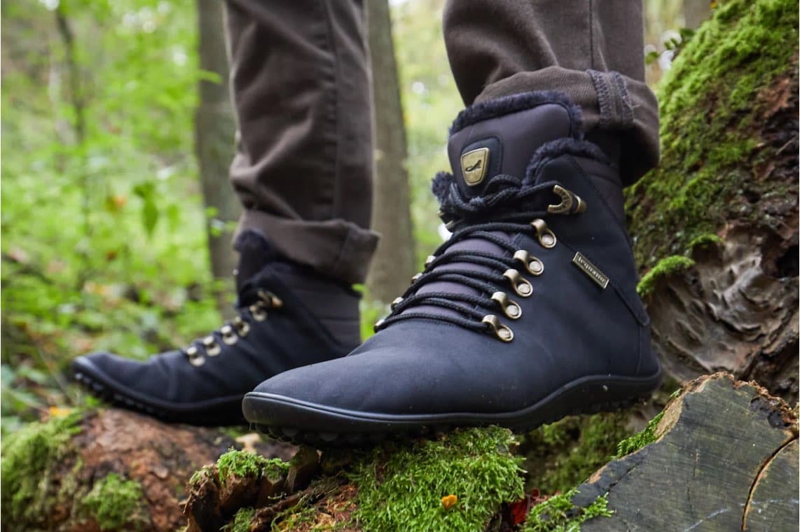 Dunkelblaue Outdoor-Schuhe an Person im Wald, ein Fuß steht auf bemoostem Baumstamm