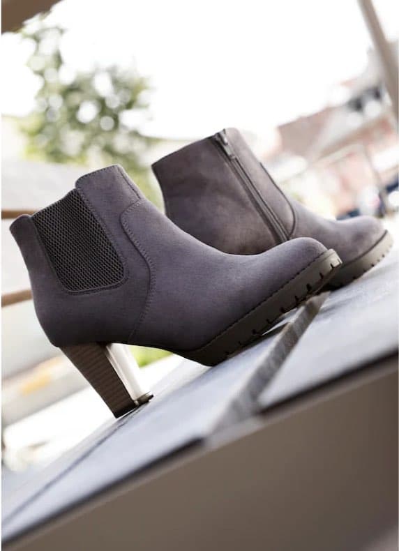 Grau melierte Stiefeletten mit Blockabsatz und Profilsohle stehen schräg auf einer Bank im Freien