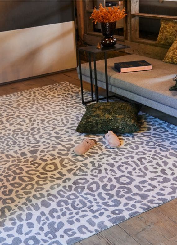 Leopardenmuster-Teppich vor Sofa, darauf grünes Kissen und rosa Hausschuhe in gemütlicher Wohnzimmerecke