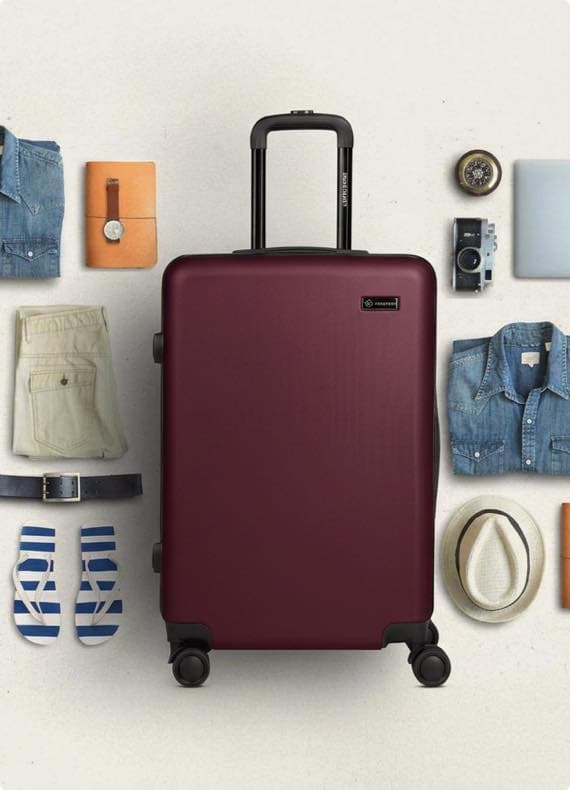 Großer Koffer mit ausgezogenem Griff, umgeben von Sommerkleidung, Hut, Sandalen, Kamera und Reiseaccessoires