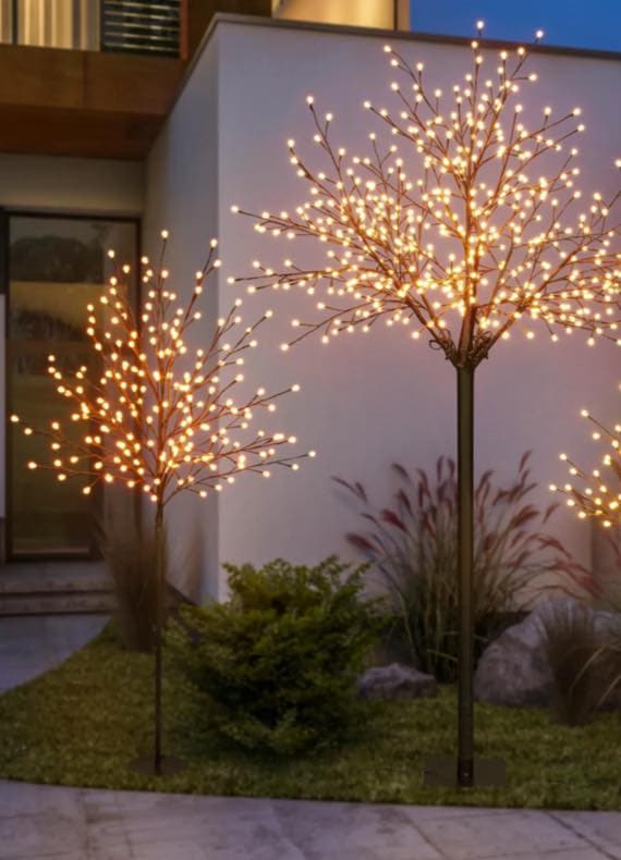 Zwei leuchtende LED-Dekobäume im Vorgarten vor einem modernen Haus bei Abenddämmerung