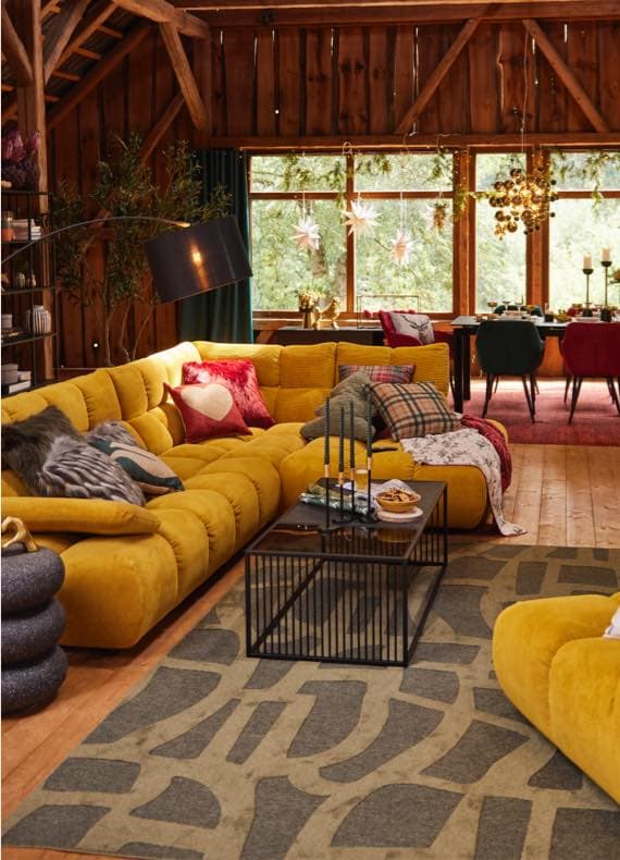 Gemütliches Wohnzimmer mit großem gelben Ecksofa, Couchtisch und Blick auf Esstisch vor großen Fenstern mit Sternendeko