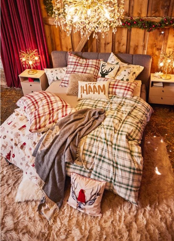 Kissen mit Schriftzug JHAAM auf weihnachtlich dekoriertem Bett mit karierten Decken und Lichterketten im Schlafzimmer
