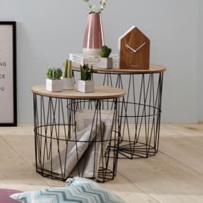 Zwei moderne Beistelltische mit runden Holzplatten und einem schwarzen Drahtgestell. Auf den Tischen stehen kleine Pflanzen in Töpfen, eine dekorative Vase und Bücher. Der Boden ist aus Holz, und im Hintergrund ist ein gerahmtes Bild zu sehen.