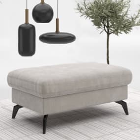 Ein eleganter Stauraum-Hocker in hellem Stoff mit gepolsterter Oberfläche und schwarzen Beinen. Im Hintergrund ist eine Zimmerpflanze zu sehen und der Boden ist mit einem hellen Teppich ausgelegt.