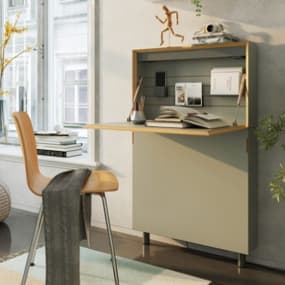 Ein modernes Wandklapptisch-System in sanften Farben, das an der Wand montiert ist. Der Tisch ist heruntergeklappt und bietet Platz für Bücher und Dokumente.