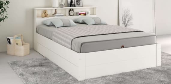 Ein modernes Bett in Weiß mit einem integrierten Kopfteil, das Regalfächer für Dekoration und persönliche Gegenstände bietet. Die Matratze ist mit einem grauen Bezug und einem gestreiften Bettlaken ausgestattet.