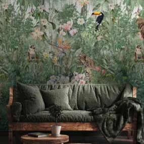 Ein gemütliches Sofa in einem tiefen Grünton, das mit einer weichen Decke und Kissen dekoriert ist. Im Hintergrund ist eine lebendige Foto-Wandtapete mit tropischen Pflanzen, Blumen und Tieren. Ein kleiner Tisch steht vor dem Sofa.
