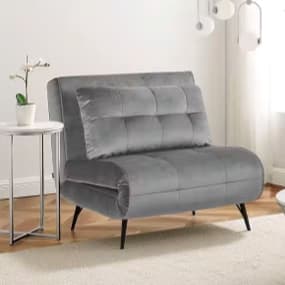 Ein eleganter, grauer, Sessel, als Tagesbett ausklappbar, mit Knopfdetails. Neben dem Sessel steht ein kleiner runder Tisch mit einer Pflanze in einer Vase. Im Hintergrund sind helle Wände und eine große Fensterfläche für eine freundliche Atmosphäre.