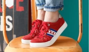 Ein Paar rote Sneakers mit weißen und blauen Streifen. Die Schuhe haben eine hohe Sohle und sind mit lässigen, hochgekrempelten Jeans kombiniert. Der Hintergrund ist in einem lebhaften Farbton gehalten.