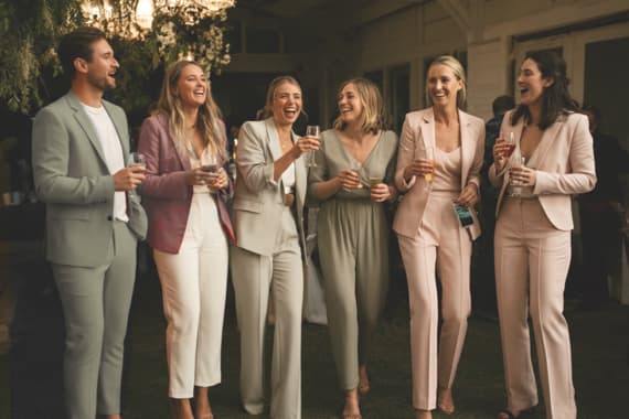 Sechs Personen in eleganter Kleidung stehen zusammen, halten Getränke und unterhalten sich in einem festlichen Ambiente.