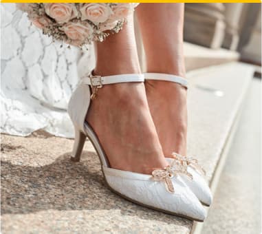 Braut in weißen High Heels mit Schleifen-Details, hält einen Blumenstrauß aus rosa und weißen Rosen