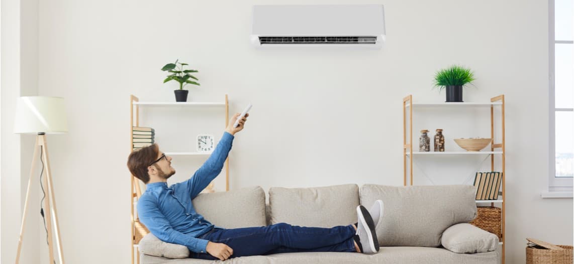 Mann sitzt auf Sofa und schaltet mit Fernbedienung eine Klimaanlage ein