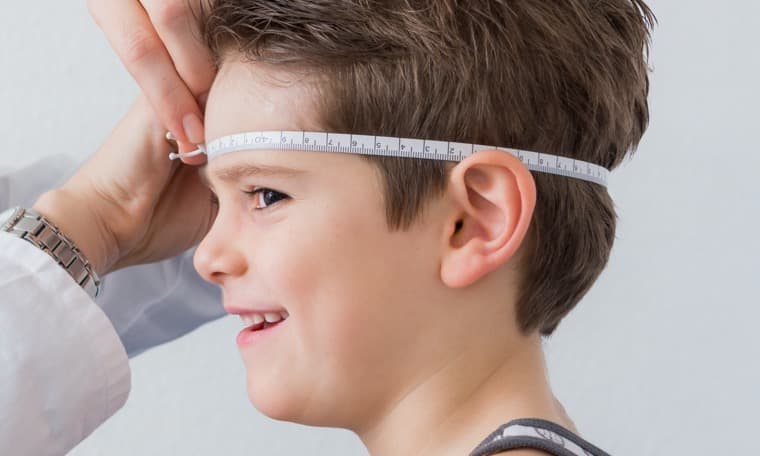 Frau mit Maßband misst den Kopfumfang eines Jungen