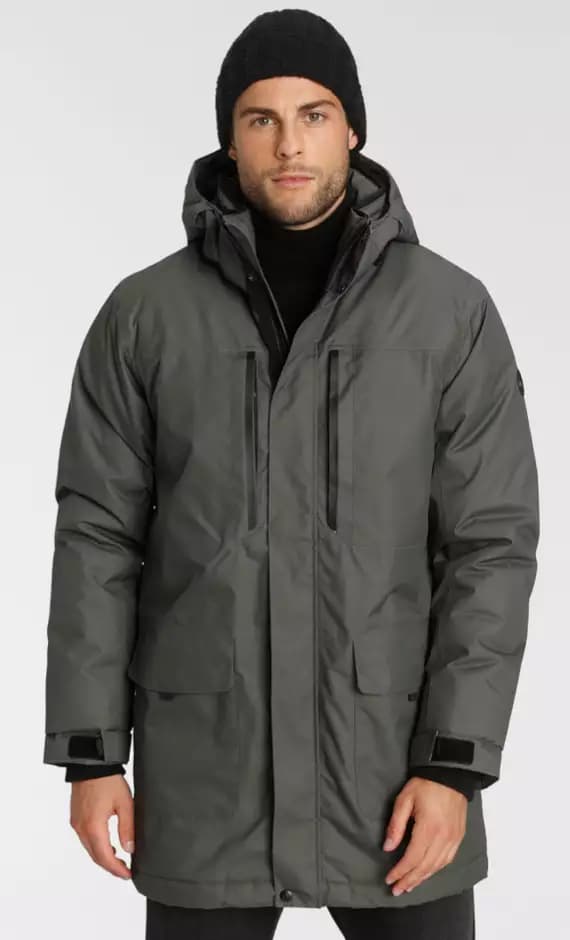 Frau trägt grünen Parka mit dunklem Schal und Wollmütze zur schwarzen Stoffhose.